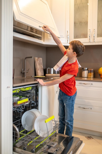 Joyous kid looking at dishware arranged on the dish drainer