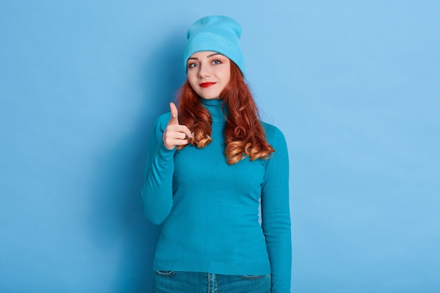 Joyous pretty European lady makes finger gun gesture to camera