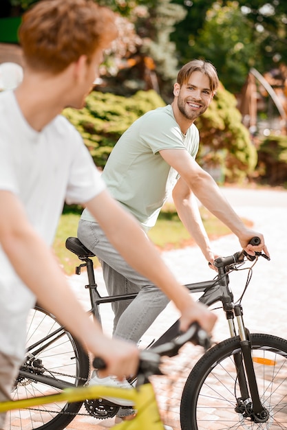 Joyous sportsman and his pal riding bikes in a park