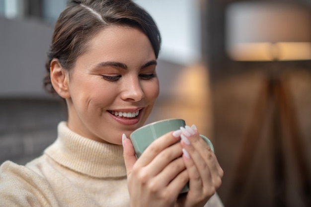 Joyous woman holding the mug with a beverage