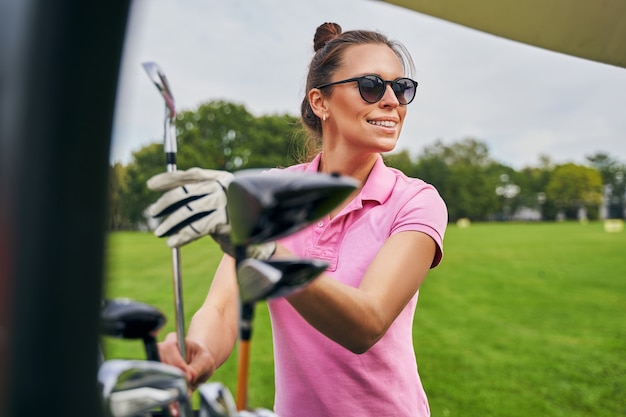 Joyous woman in a polo shirt holding a wedge club with both\
hands