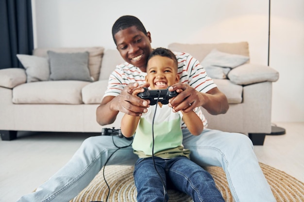 Joysticks gebruiken om videogame Afro-Amerikaanse vader met zijn jonge zoon thuis te spelen