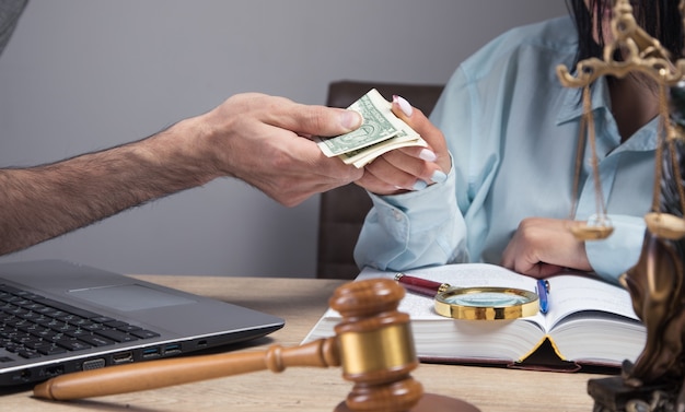 The judge accepts a bribe sitting in front of a hammer and a statue of justice