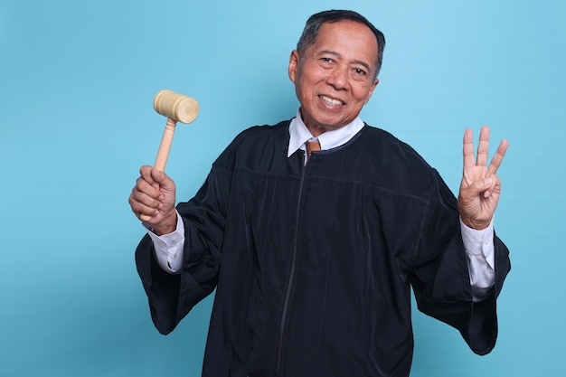 裁判官のアジア人男性が笑みを浮かべて、青い背景に分離された指で 3 つ数える