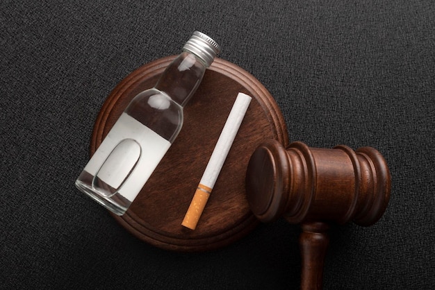 Judge gavel next to cigarettes and bottle of alcohol Alcohol and Tobacco Law Top view