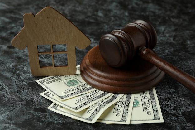 Judge gavel, dollars and wooden house on black smokey table