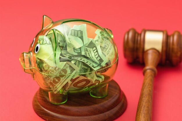 Judge gavel and transparent piggy bank full of money on a red background