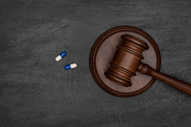 Judge gavel and two pills. Illegal use of drugs. Pharmaceutical lawsuit. Black surface.