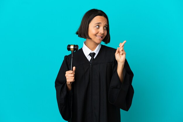 Judge over isolated blue background with fingers crossing and wishing the best