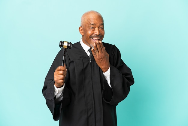 Judge senior man isolated on blue wall happy and smiling covering mouth with hand