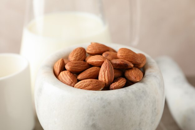 Jug of almond milk, mortar with almond seeds on brown table, closeup