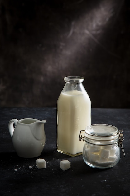 A jug / bottle of milk and a sugar pot on black table