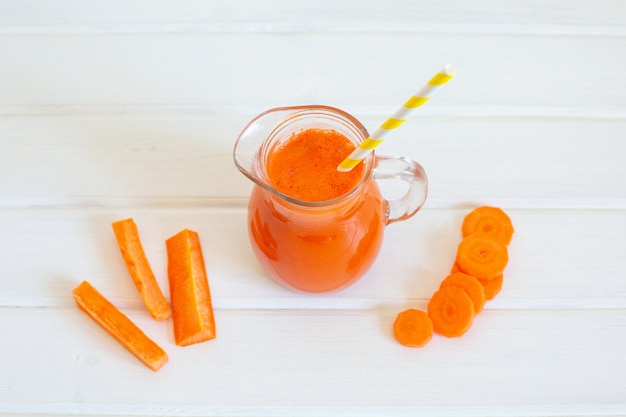 Foto brocca di succo di carota e carote fresche su su sfondo bianco.