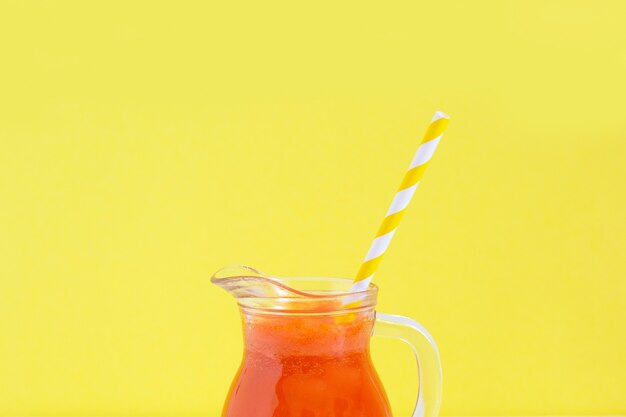 Jug of carrot juice with cocktail tube on yellow background. Healthy detox eating, alkaline diet. Summer food concept.