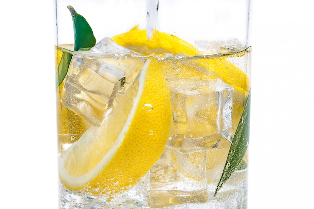 용기에는 얼음 음료, 신선한 육즙이 많은 노란색 레몬 및 맑은 물의 소엽이 있습니다.