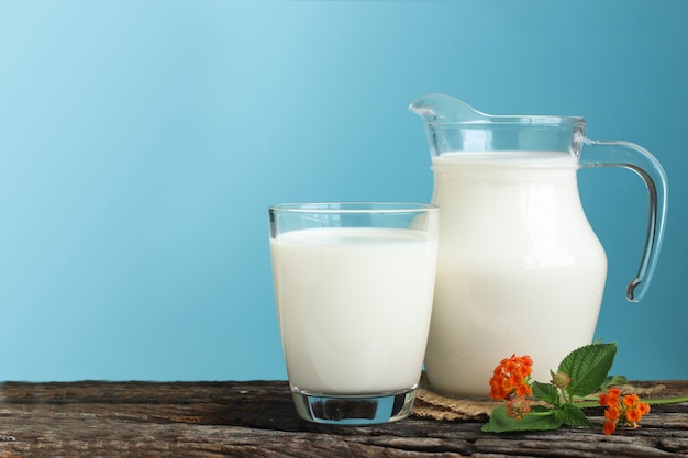 A jug of milk and glass of milk on a wooden table on a blue background.