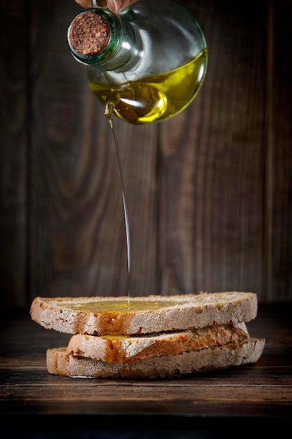 Brocca di olio d'oliva che gocciola sopra fette di pane bianco