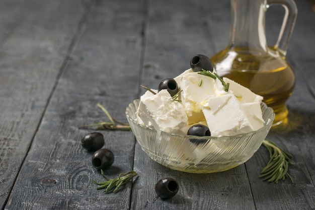 A jug of olive oil and feta cheese with olives on a wooden table. Natural cheese made from sheep's milk.