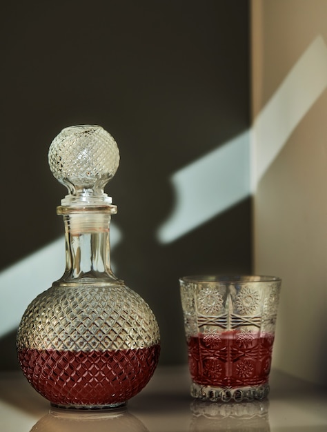 Jug of red wine and glass of wine, with unusual lighting in the form of patterns on the wall.