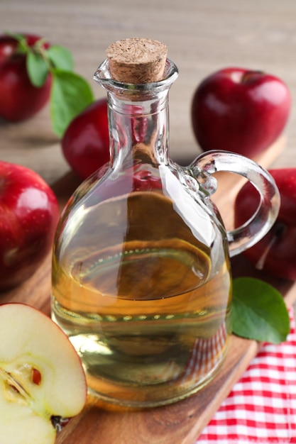 Jug of tasty juice and fresh ripe red apples on wooden table closeup