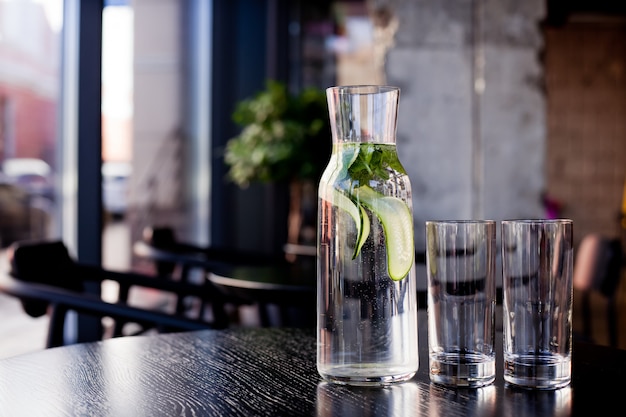 Jug of water with cucumber and mint and two empty glasses on a table in a restaurant