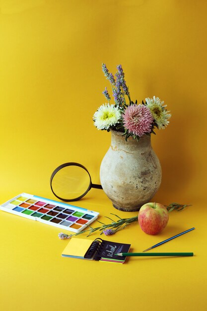 Jug with flowers apple stationery on the table bright background learning concept