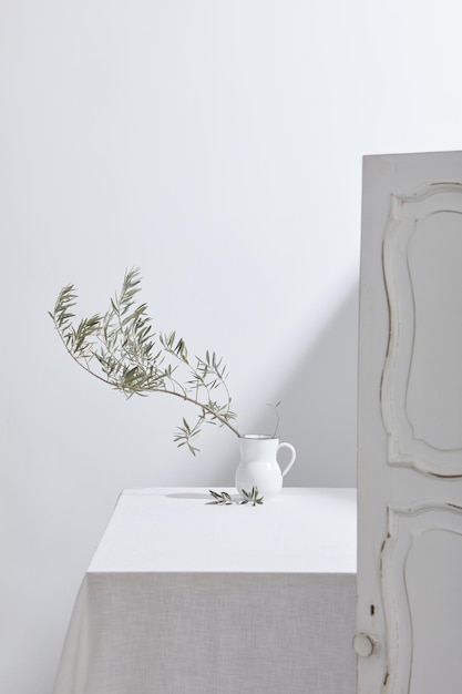 Jug with olive branch on white table and copy space