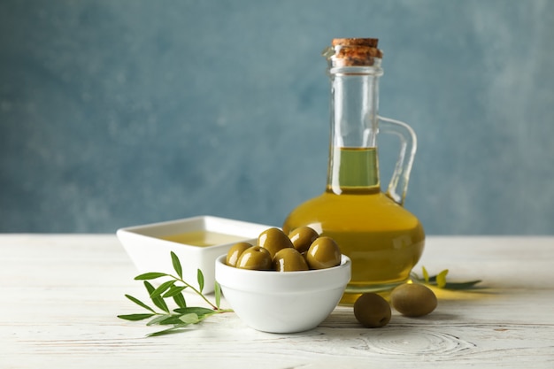 Jug with olive oil and bowl with olives on wooden table, space for text