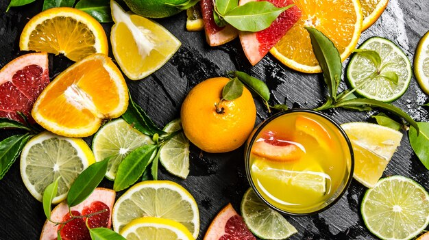 Succo di agrumi. pompelmo, arancia, mandarino, limone, lime in vetro sulla tavola di legno nera. vista dall'alto