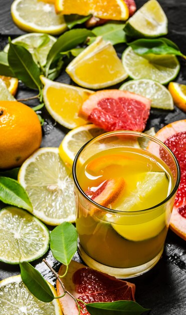 juice from citrus fruits. grapefruit, orange, tangerine, lemon, lime in glass on black wooden table.