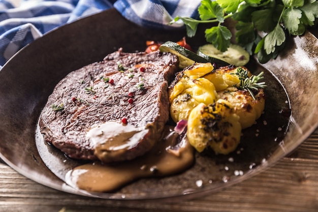 Foto succosa bistecca di manzo rib eye patate arrosto con salsa di verdure grigliate sale pepe ed erbe aromatiche in padella vintage.