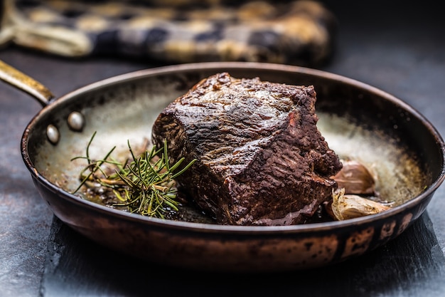 Juicy beef steak with spices and herbs in old pan.