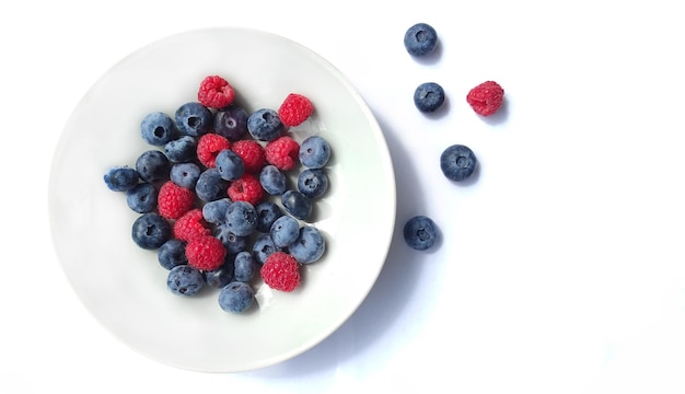 Juicy blueberries and raspberries in a plate close-up on a white background