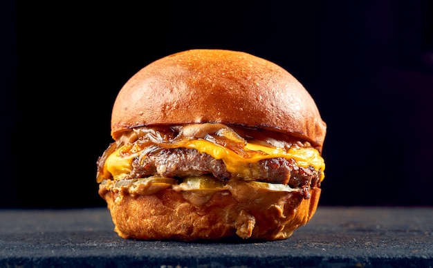 Hamburger succoso con manzo, formaggio, cipolle caramellate e pomodoro, salsa su fondo scuro.