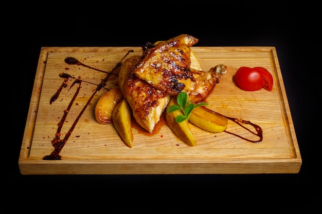 Juicy chicken in a sauce with baked apples, tomatoes and herbs. Hearty dish on a wooden board, on black background. Copy space