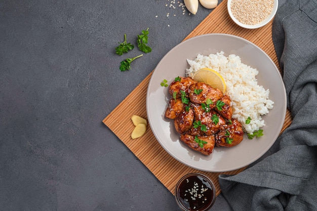 Juicy chicken in Teriyaki sauce served with rice, sesame and lemon on a brown background. Japanese Oriental cuisine. Top view, copy space.