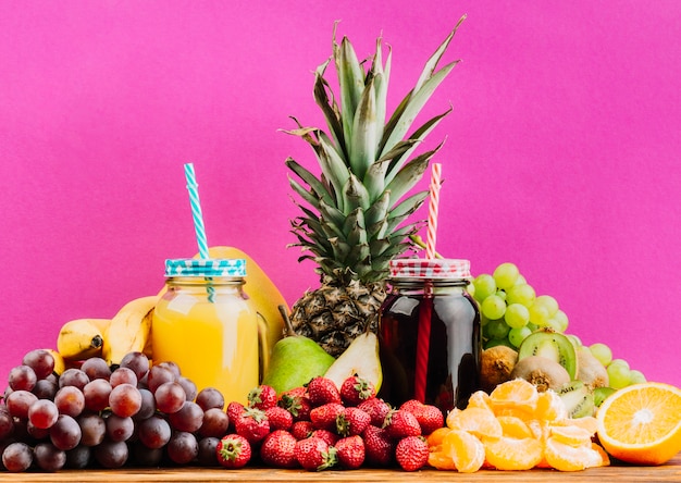 Photo juicy colorful fruits and juice mason jars against pink background