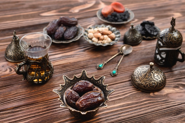 Photo juicy dates in arabian iron bowl with tea glass on wooden desk