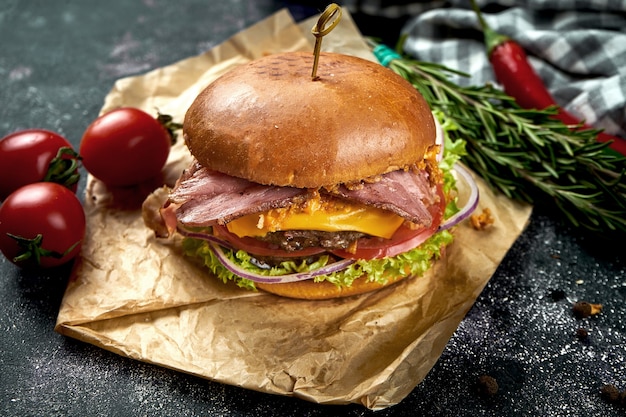 Doppio hamburger succoso con carne di manzo, pomodori pancetta, formaggio e cipolle croccanti su un tavolo scuro.