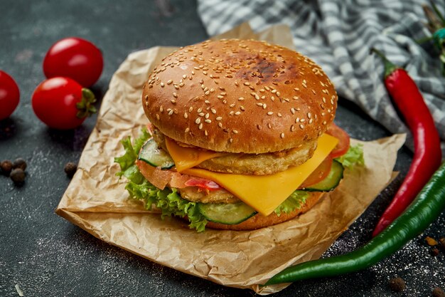 Juicy double burger with chicken, tomatoes, cheese and crispy onions on a dark table. Chickenburger