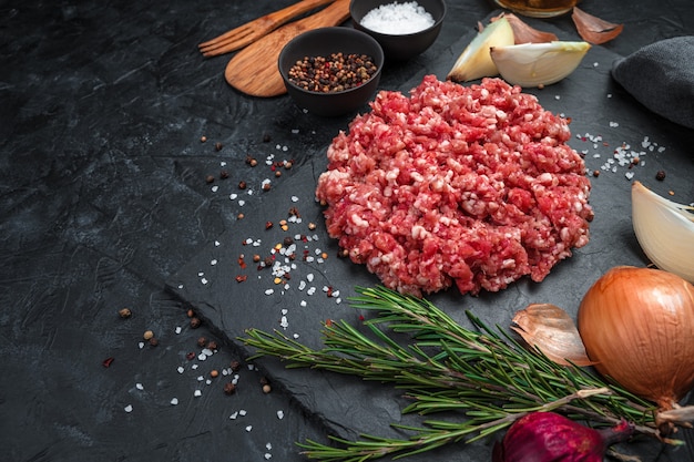 Juicy, fresh minced meat with spices on a flat plate on a black background.