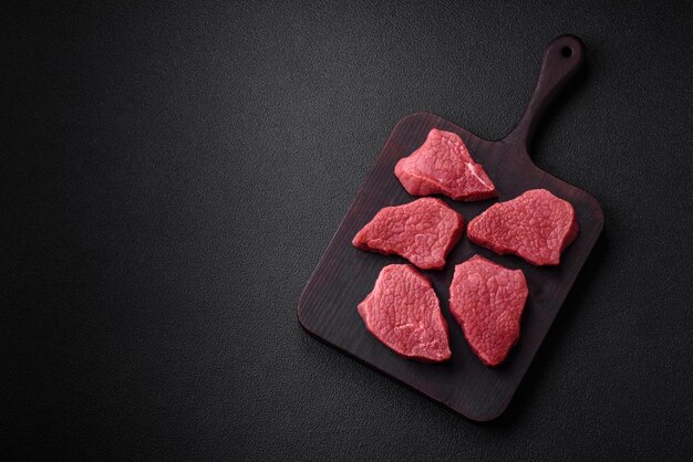 Juicy fresh raw beef meat with salt spices and herbs on a dark textured concrete background