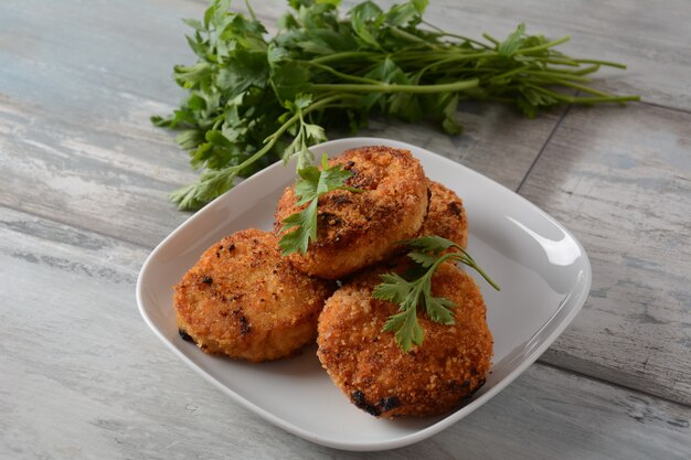 Cotolette di pollo fatte in casa fritte succose. rivestito di pangrattato, delizioso, in piatto bianco alle erbe. su fondo in legno vecchio, stile rustico