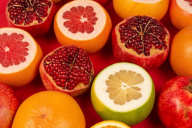 ジューシーなグレープフルーツ、オレンジ、ザクロ、赤い背景に柑橘系の甘いもの。