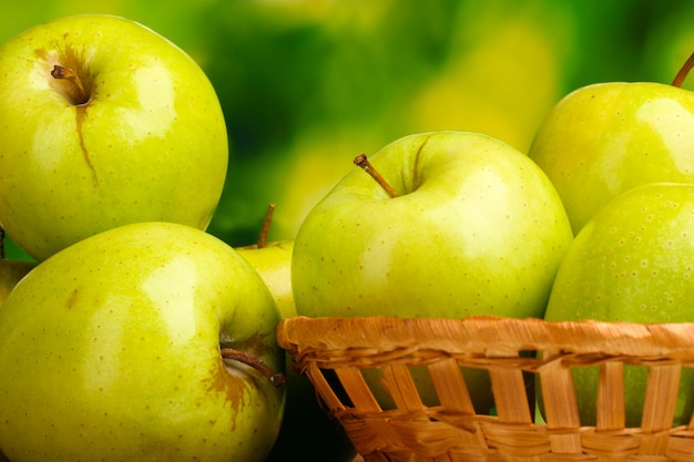 Juicy green apples in basket on green background