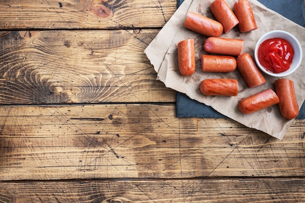 Juicy grilled half meat sausages with tomato sauce and ketchup on a wooden background. Fat fast food. Concept unhealthy eating. Copy space