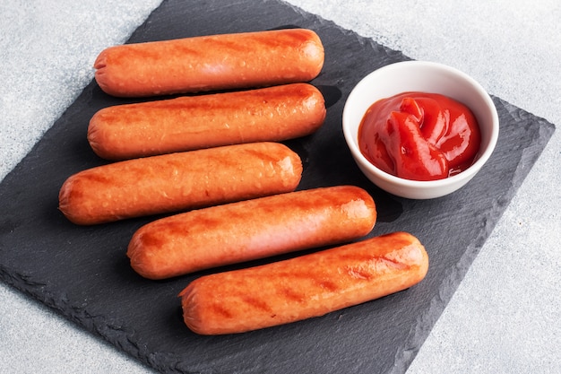 Juicy grilled meat sausages with tomato sauce and ketchup on a concrete stand. Fat fast food. Concept unhealthy eating.