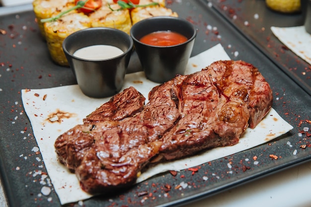 두 가지 소스가 든 육즙 구이 고기 스테이크는 검은 사각형 접시에 앉아 있습니다. 뜨거운 고기 요리.