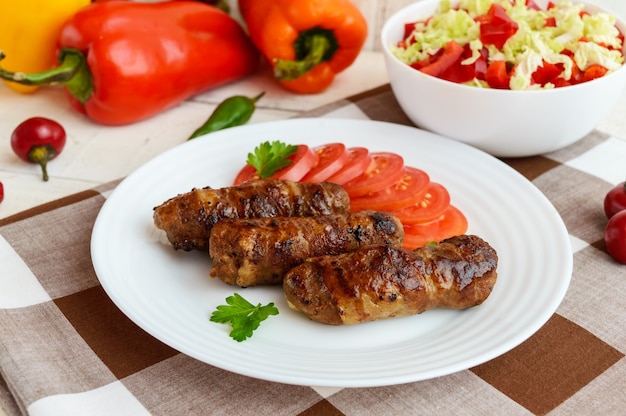 Juicy grilled rolls of minced meat wrapped in bacon with fresh tomato