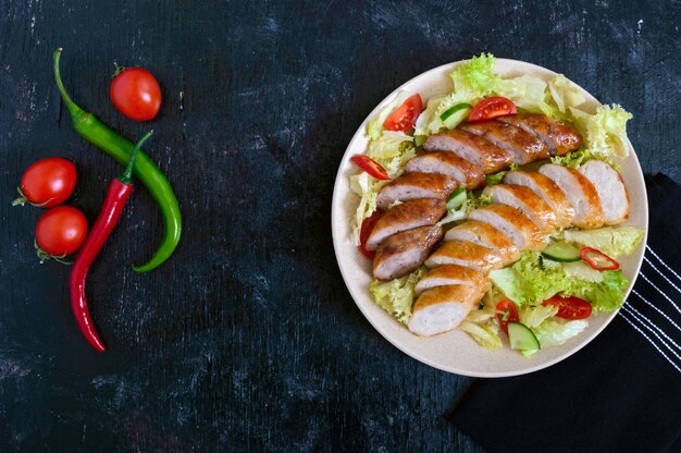Juicy home made sausage with a light spring salad of fresh vegetables on a black wooden background. A traditional Easter dish. Top view.